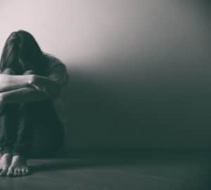 foto in bianco e nero di una donna triste per terra appoggiata ad un muro
