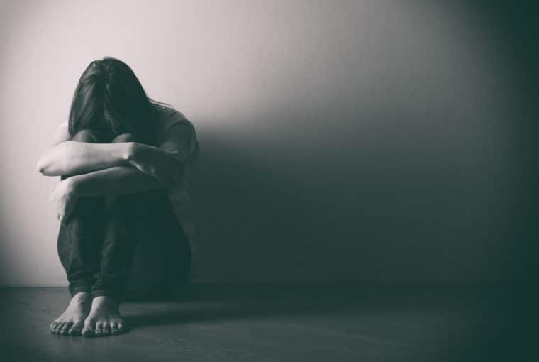 foto in bianco e nero di una donna triste per terra appoggiata ad un muro