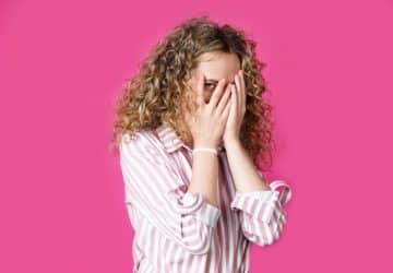 donna che si copre la faccia con le mani e spia da un occhio