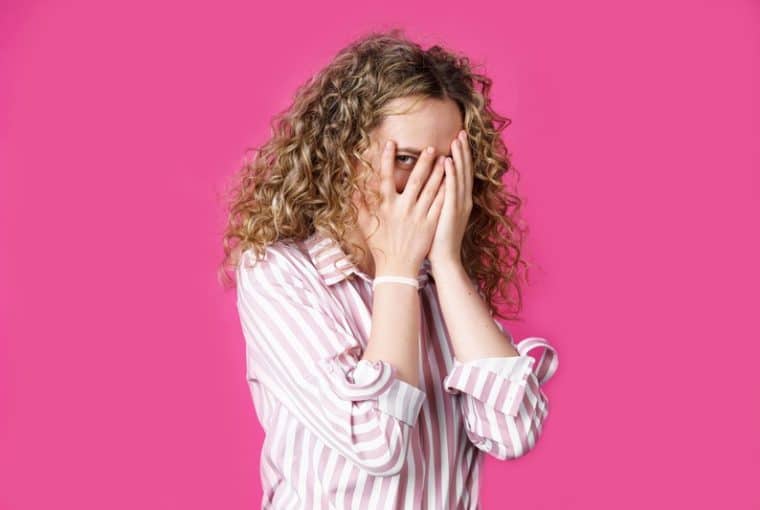 donna che si copre la faccia con le mani e spia da un occhio